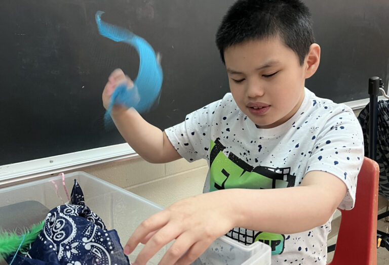 Image child playing with toy at school in front of chalkboard.