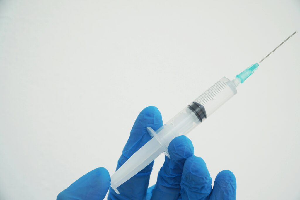 Close-up of gloved hands holding syringe on white background, ideal for medical and healthcare concepts.