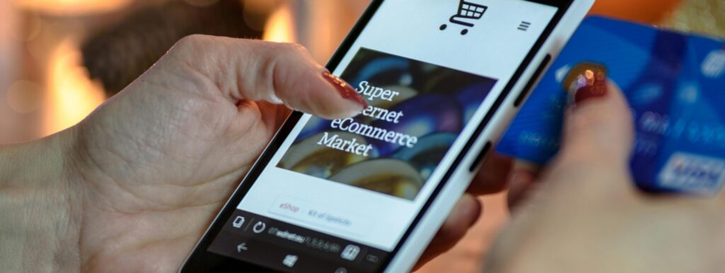 Woman using smartphone for online shopping with credit card in hand, festive background lighting.