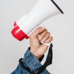 A person in a denim jacket holds a red and white megaphone, emphasizing communication.