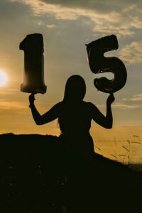 Silhouetted woman holding '15' balloons against a sunset backdrop, symbolizing celebration.