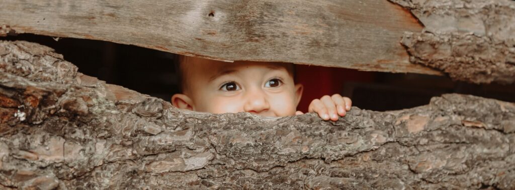 Cute baby face peeking through rustic wooden planks. Natural textures and playful expression.